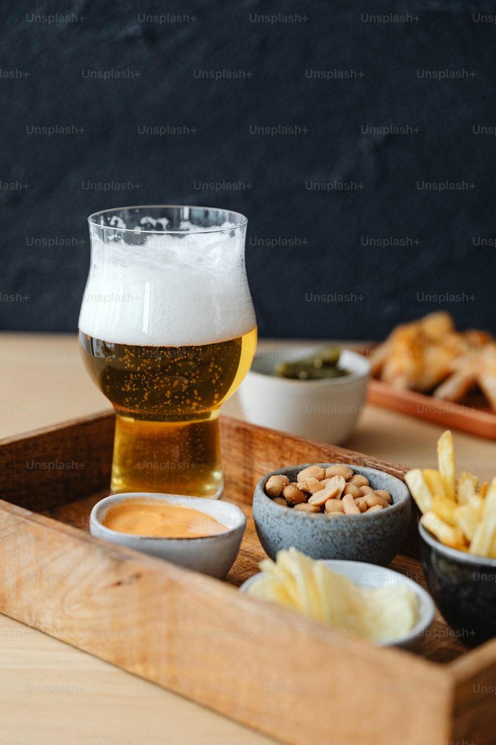 a wooden tray topped with bowls of food and a glass of beer