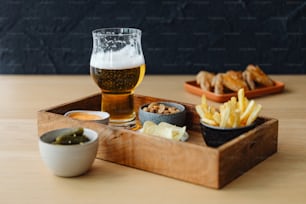 un vassoio di legno sormontato da un bicchiere di birra accanto a una ciotola di patatine fritte