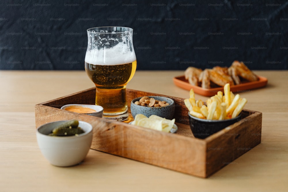 a wooden tray topped with a glass of beer next to a bowl of fries