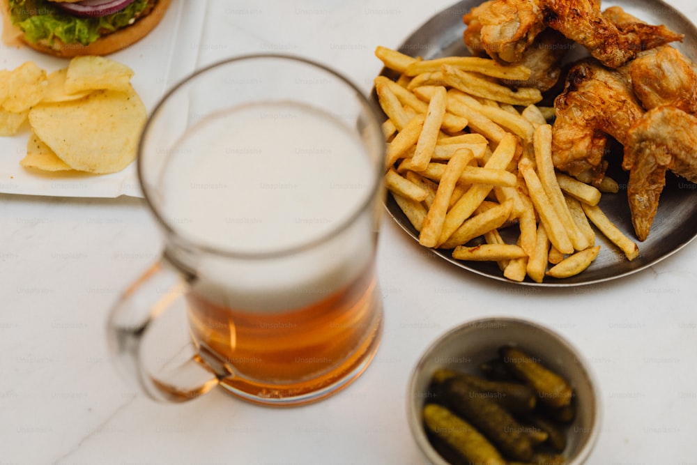 a plate of chicken wings, french fries, pickles and a glass of beer