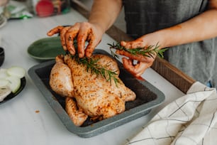 a person putting herbs on a chicken in a pan