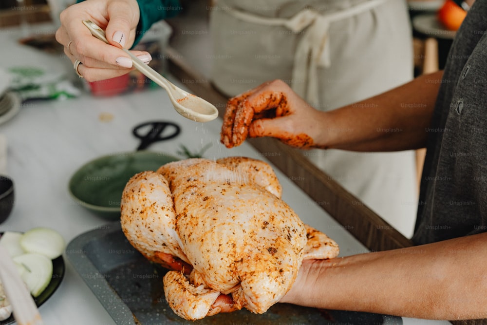 a person holding a spoon over a chicken on a pan