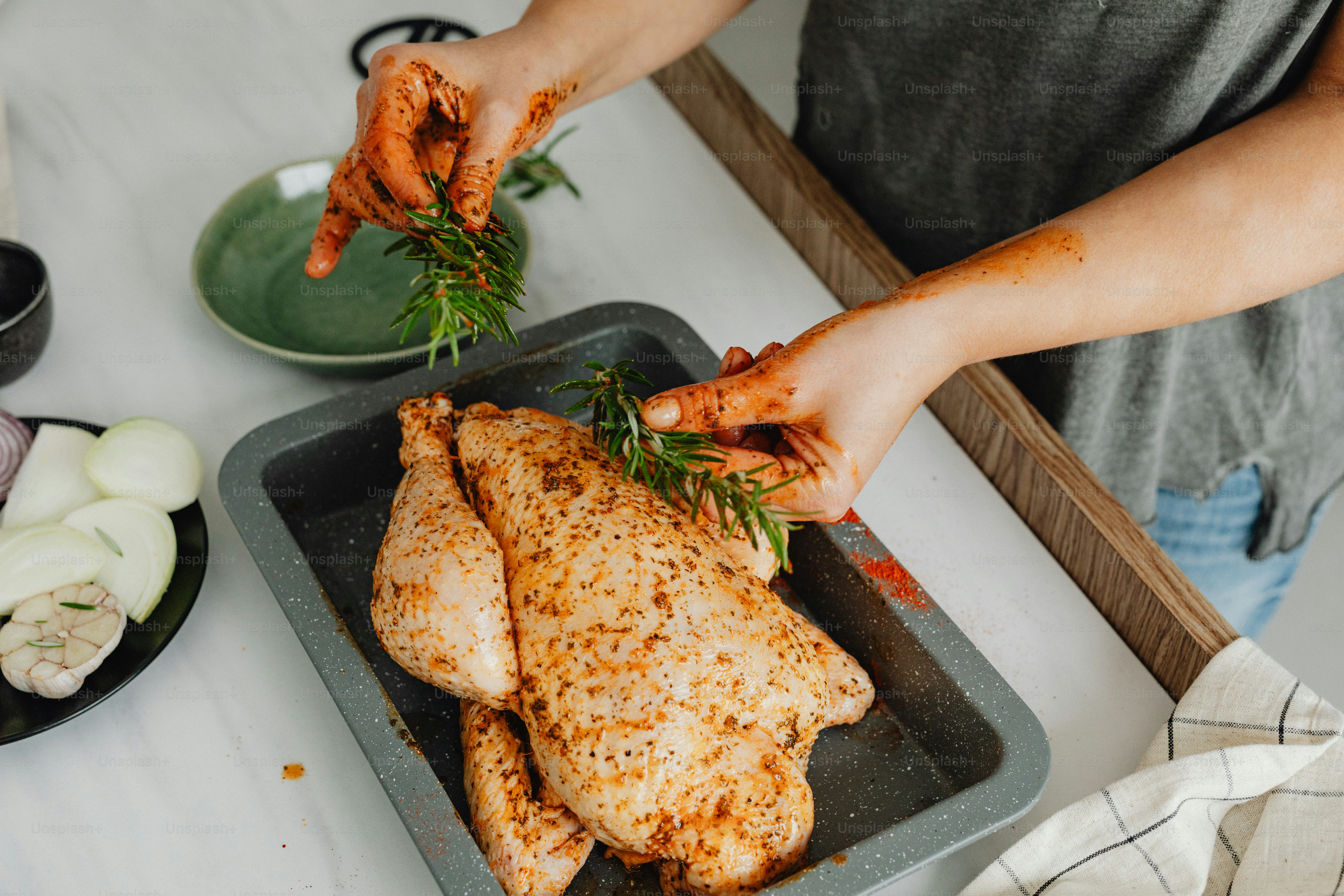 a person putting herbs on a chicken in a pan