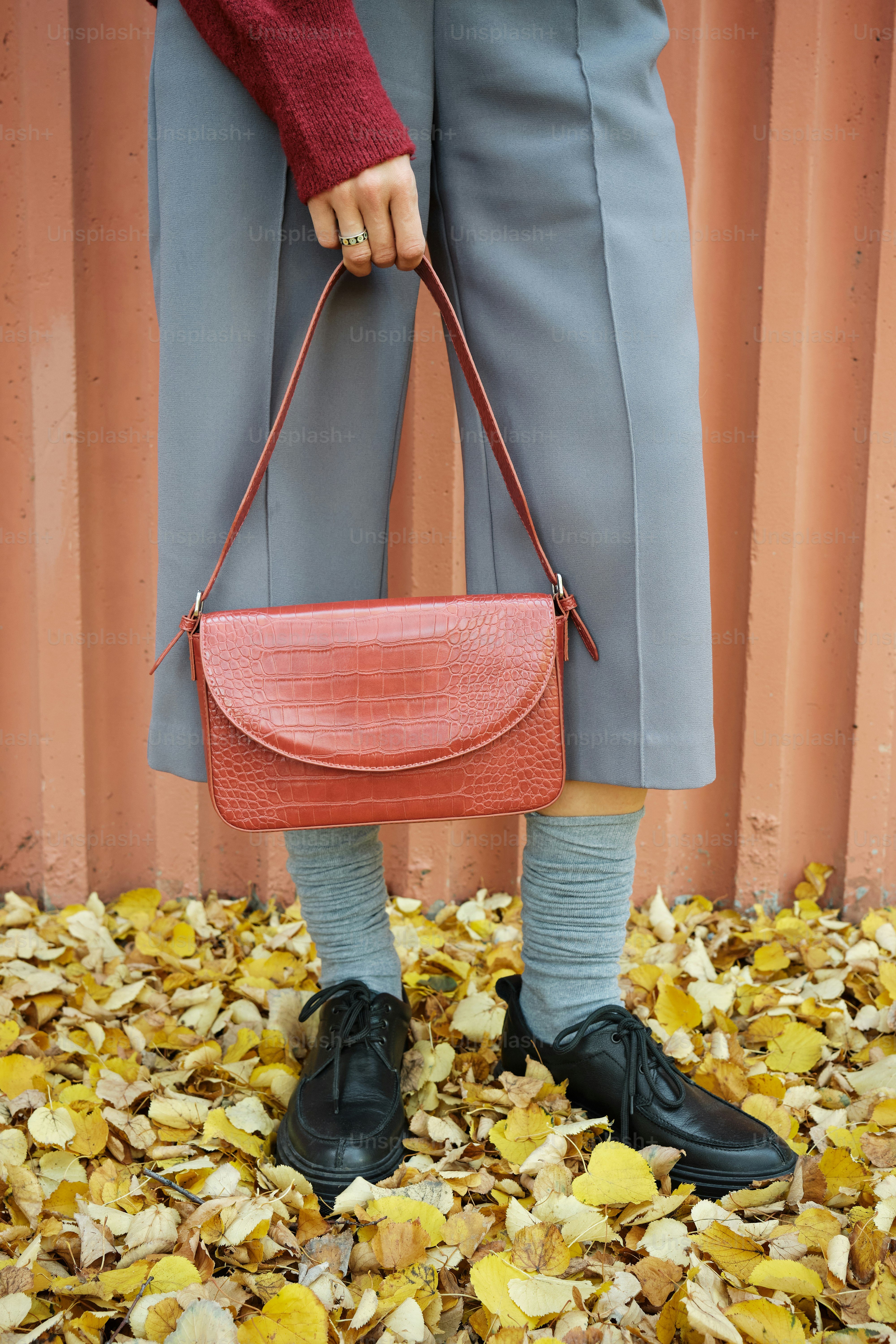 eine frau, die eine rote handtasche über einen haufen blätter hält