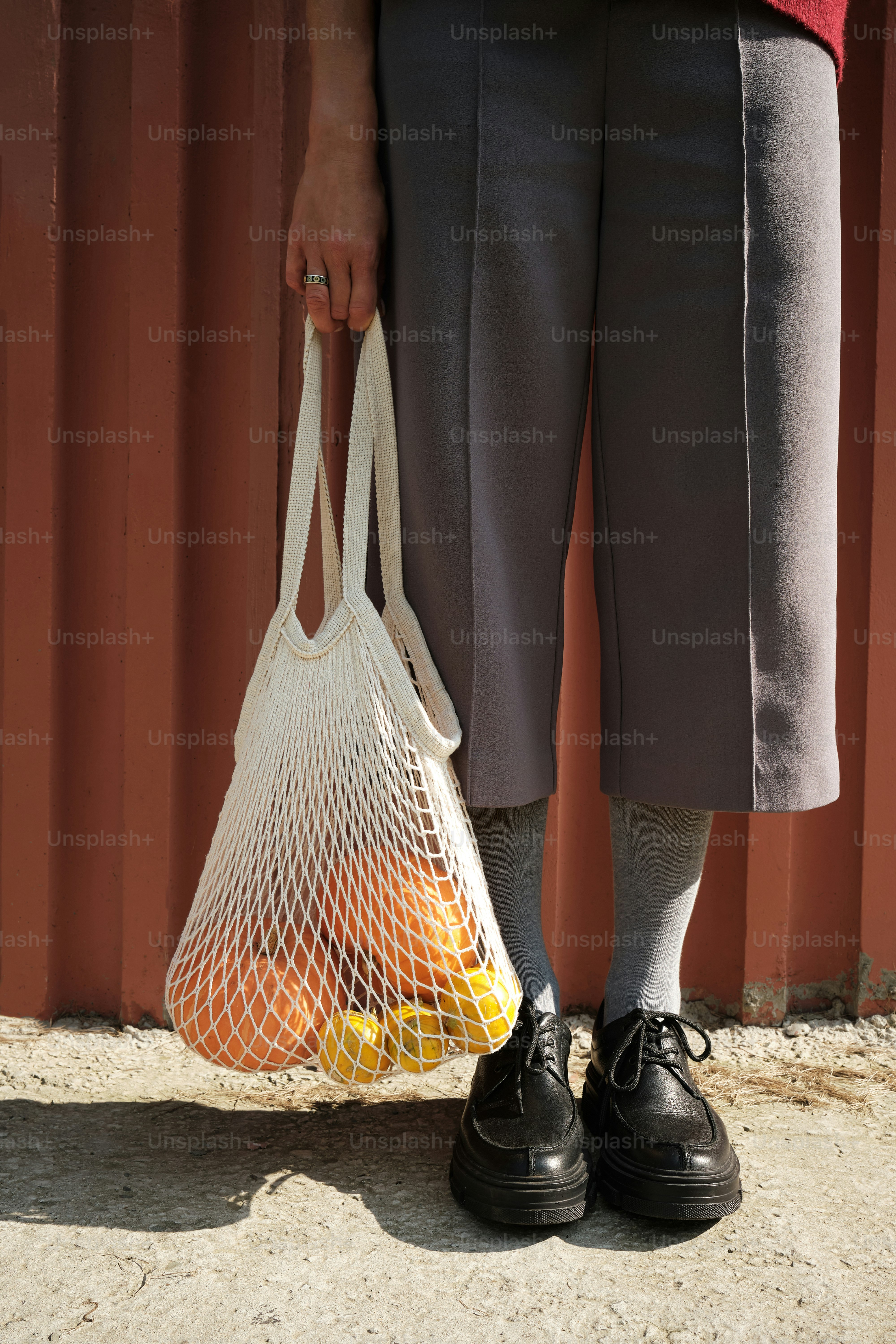 eine Person, die einen Netzbeutel mit Orangen darin hält