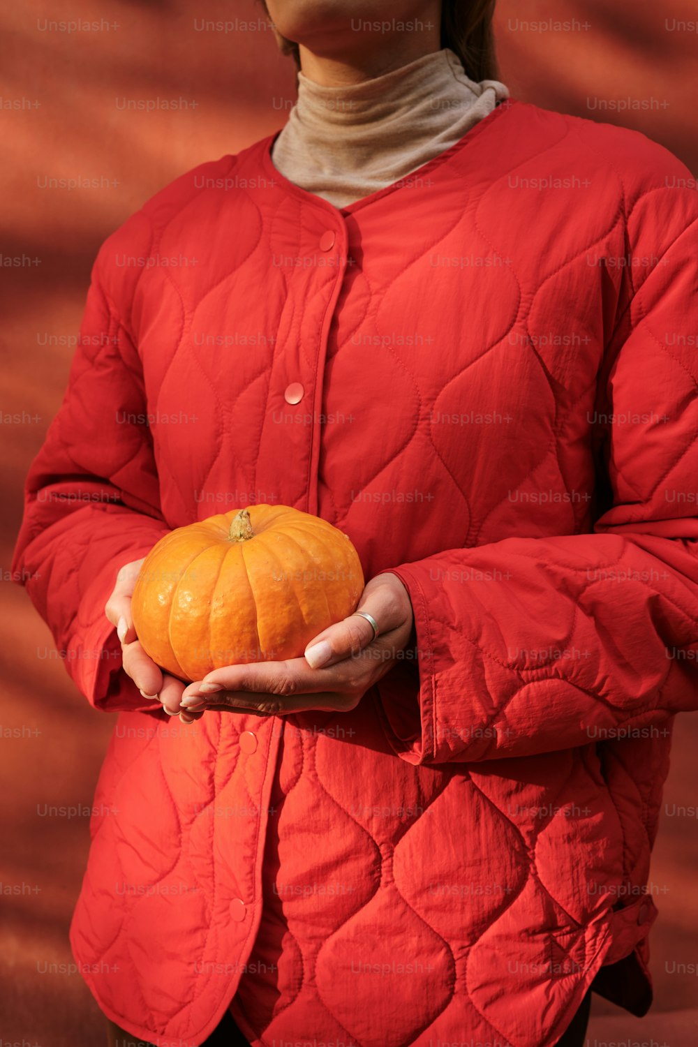a woman in a red jacket holding a pumpkin