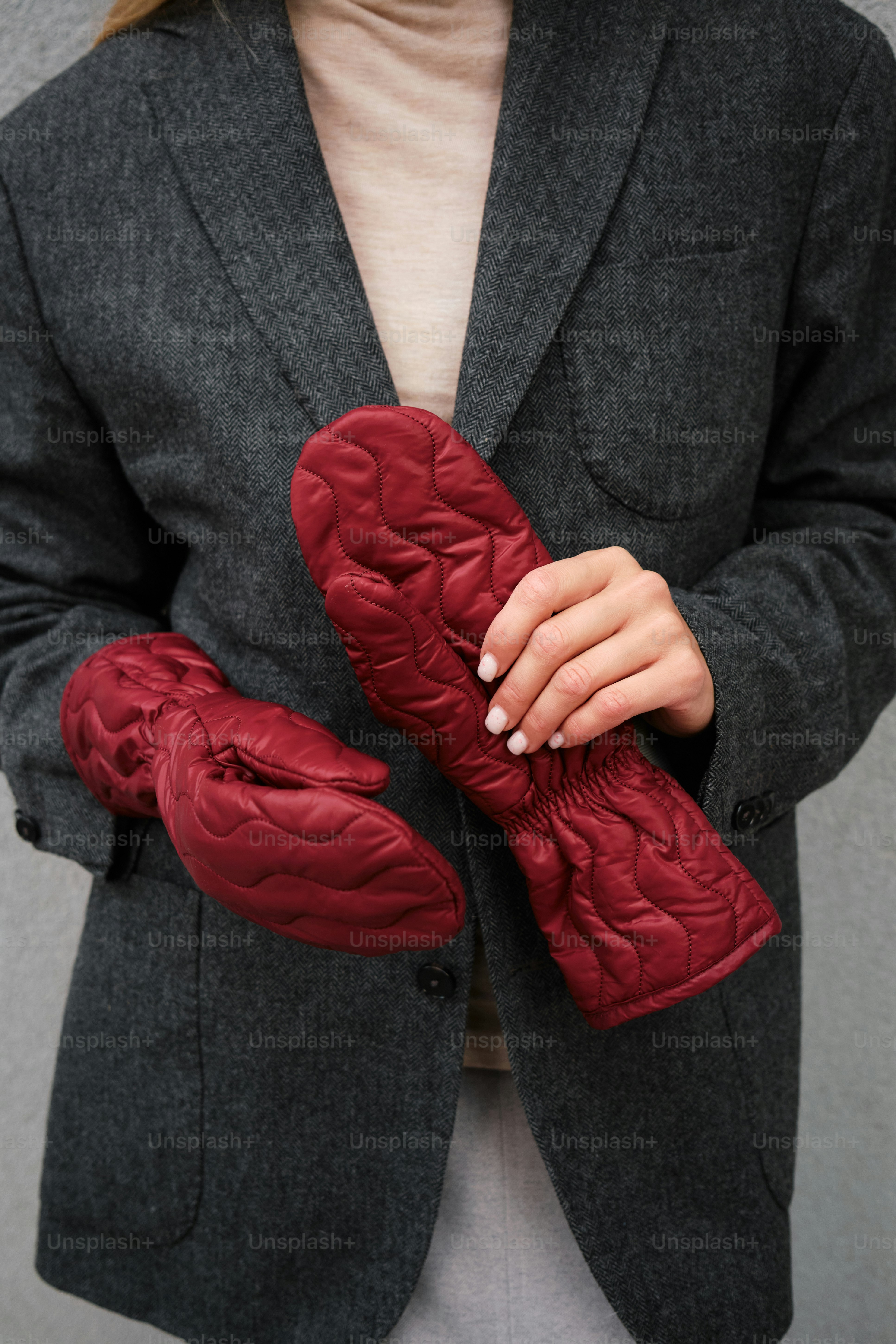une femme en veste grise tenant une paire de gants rouges