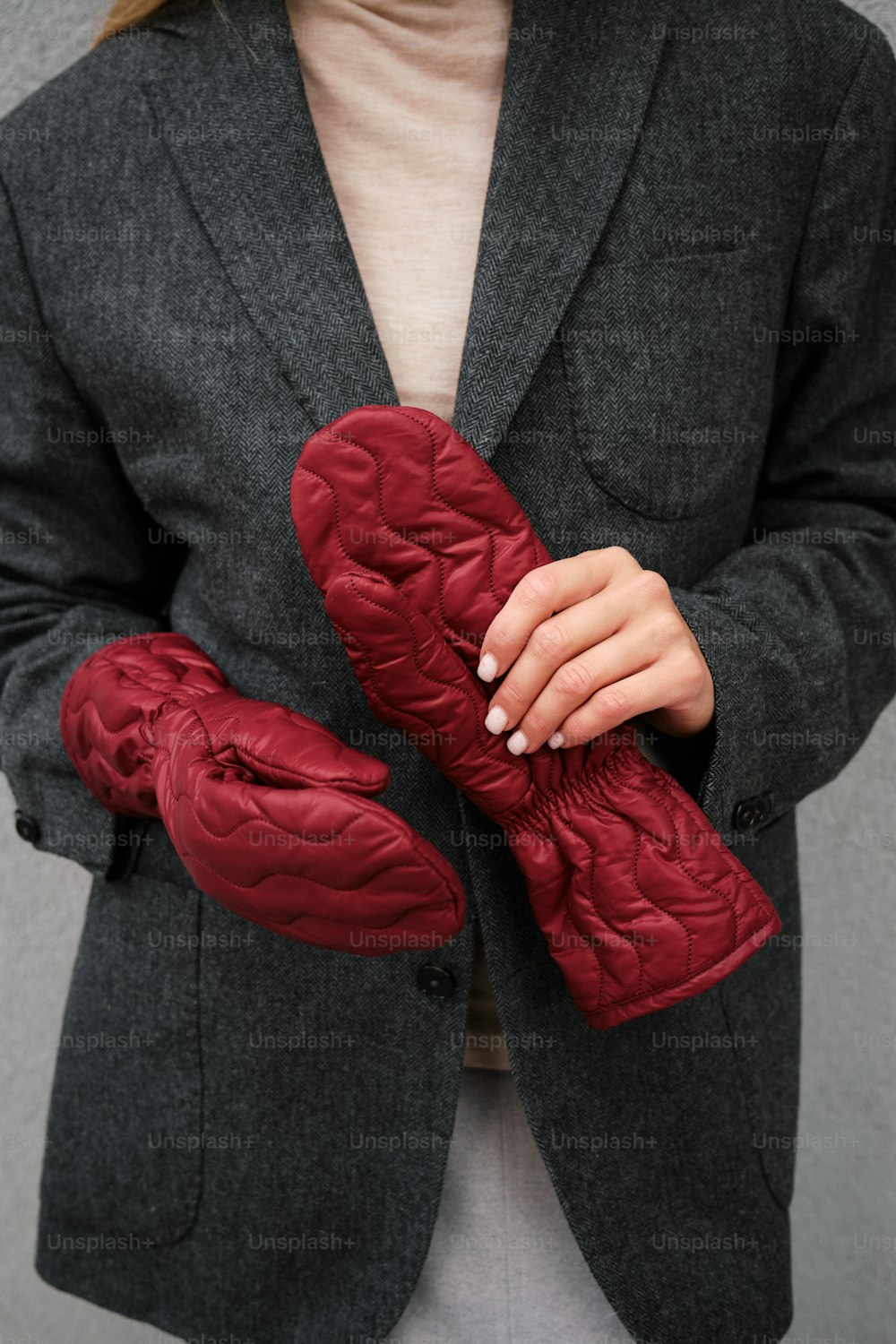 a woman in a gray jacket holding a red pair of gloves