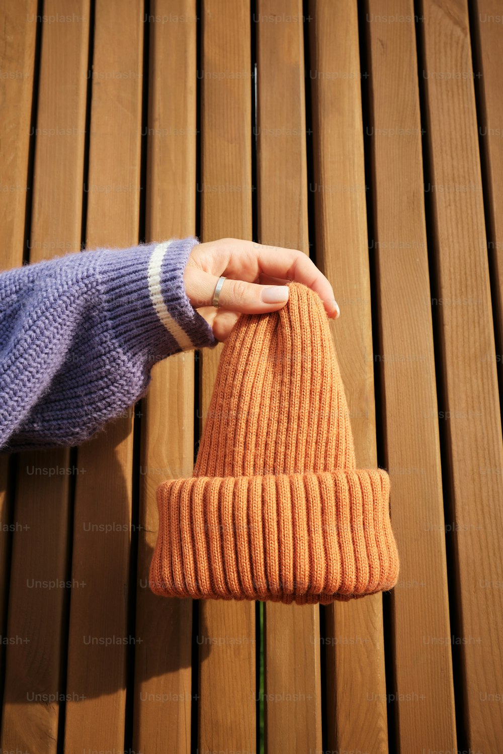 Die Hand einer Person, die eine gestrickte orangefarbene Mütze hält