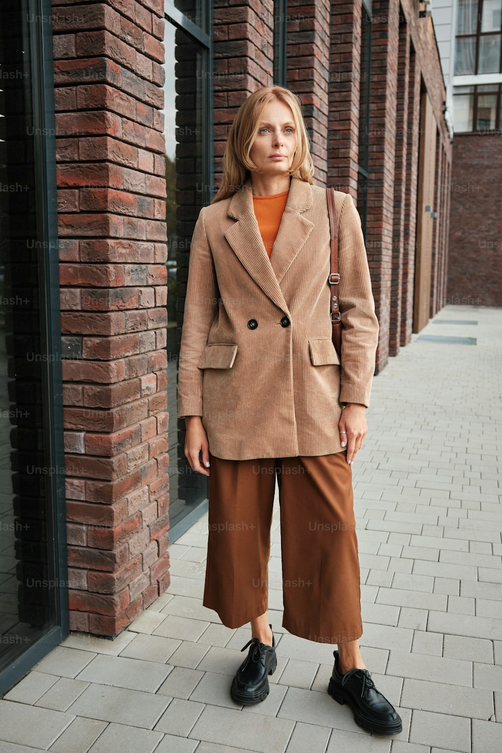 a woman standing on a sidewalk wearing a tan coat