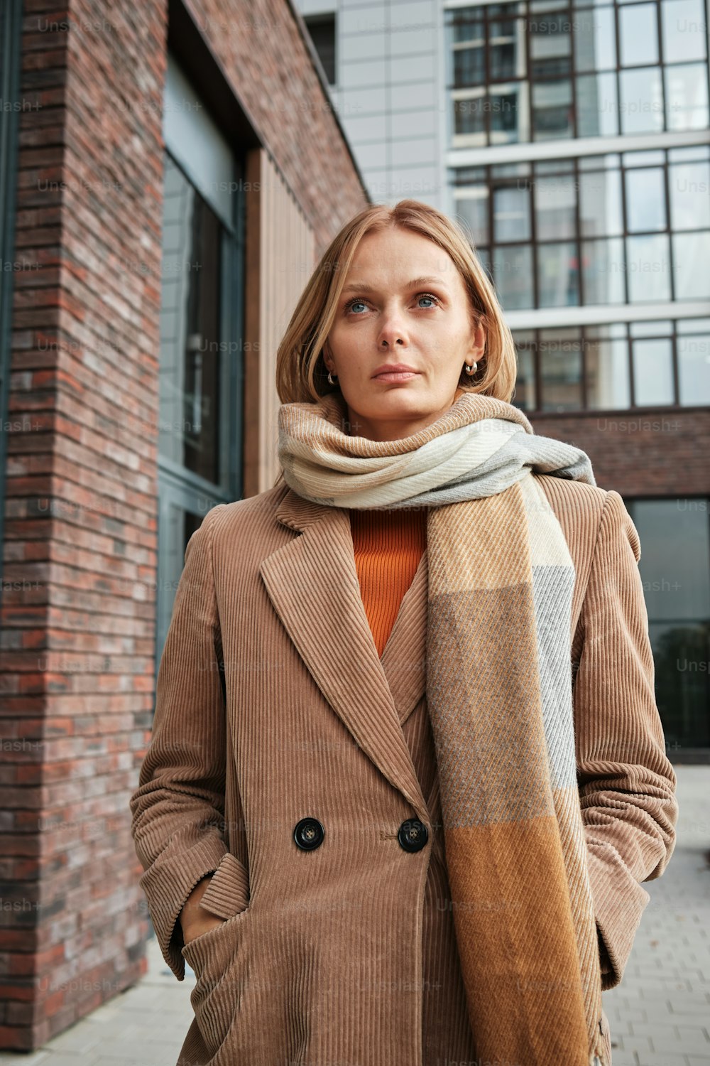 a woman wearing a coat and scarf standing in front of a brick building