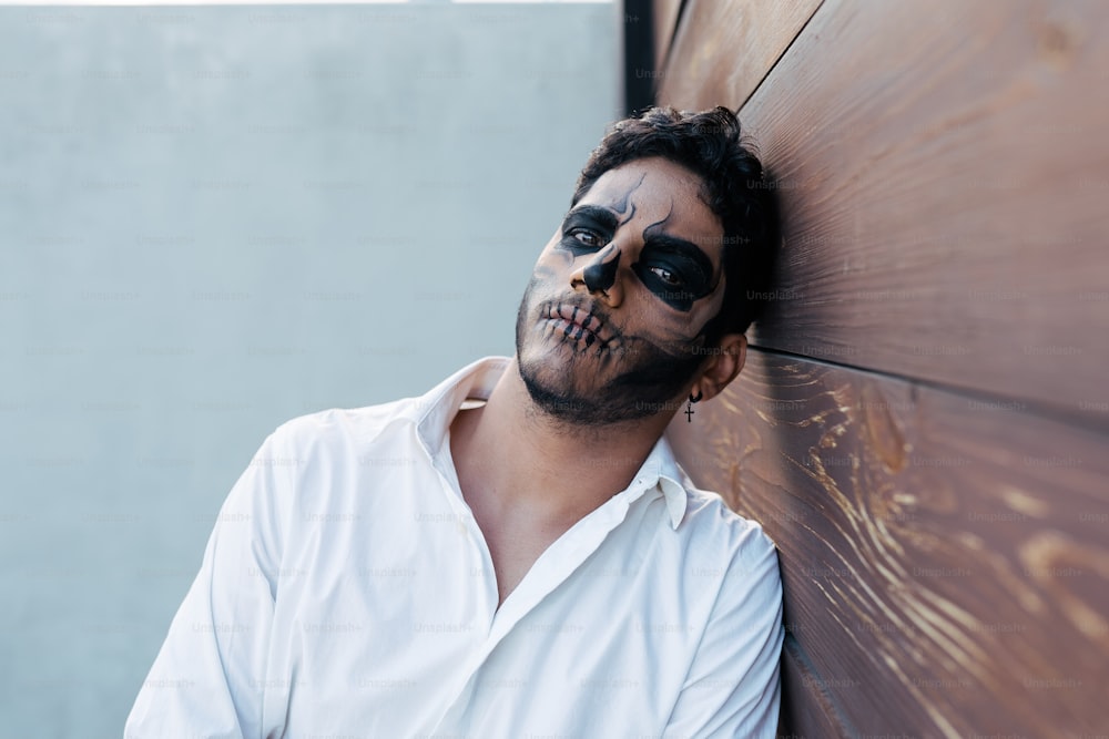 Ein Mann mit einem Skelettgesicht, das auf sein Gesicht gemalt ist, lehnt sich an eine Wand