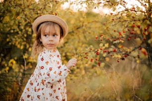 a little girl wearing a hat and holding a branch