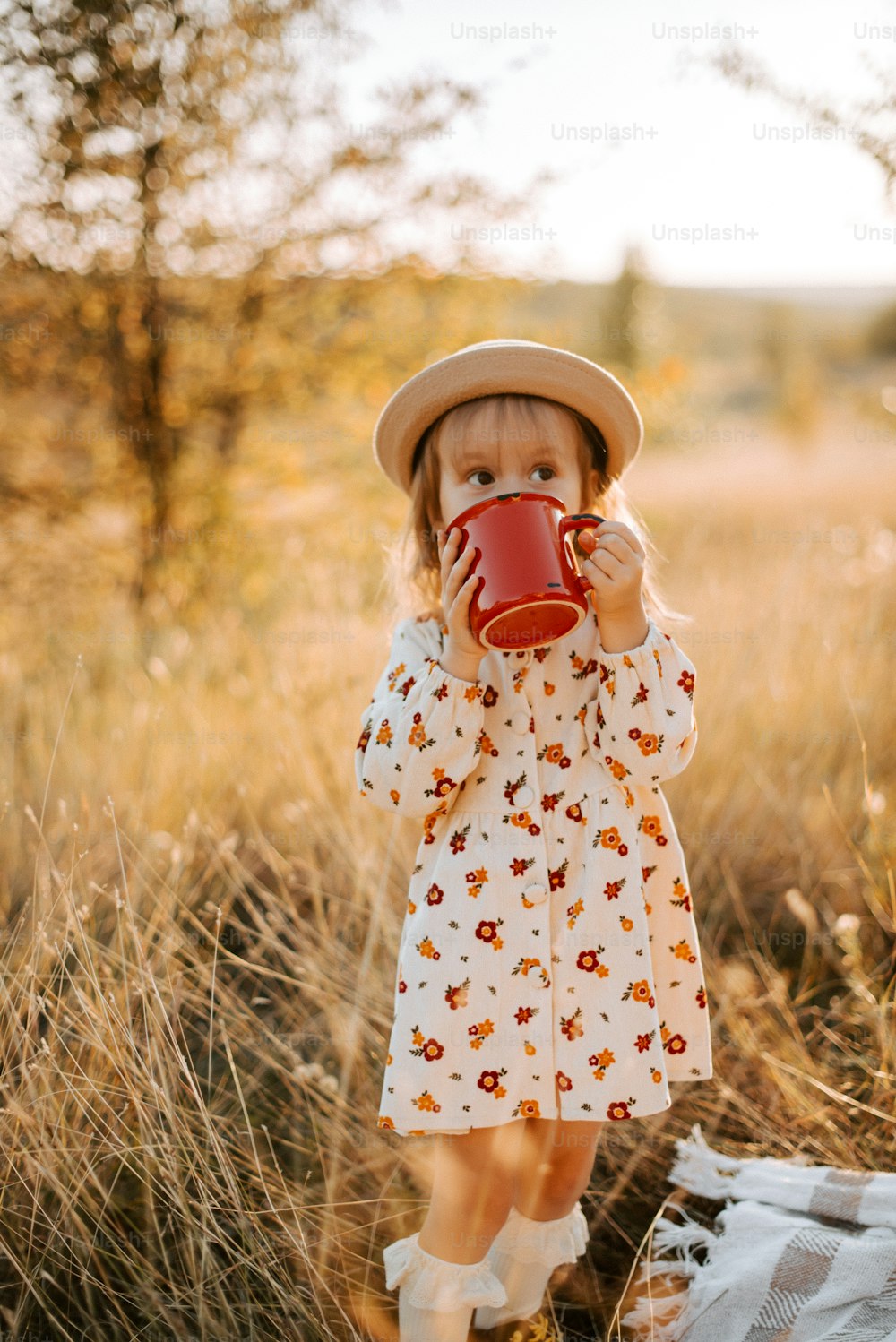 una bambina che indossa un cappello e tiene in mano una tazza rossa