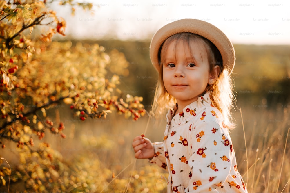 a little girl wearing a hat standing in a field