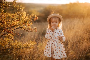 a little girl standing in a field with a hat on