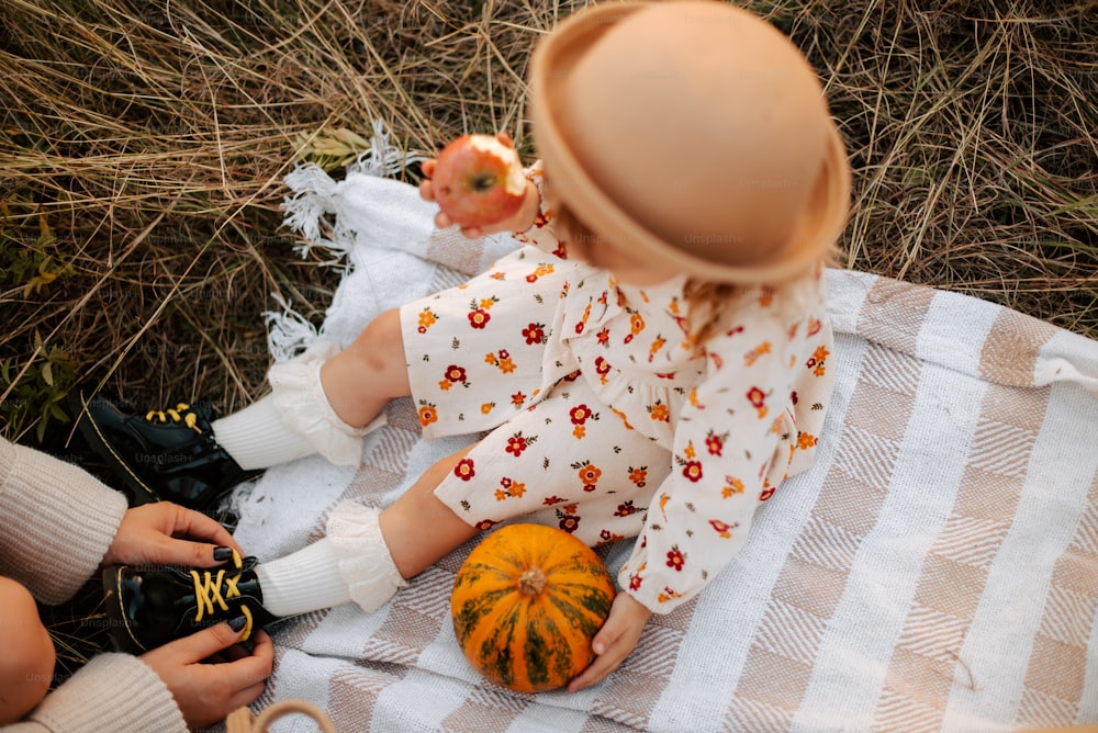 a little girl sitting on top of a blanket next to a pumpkin