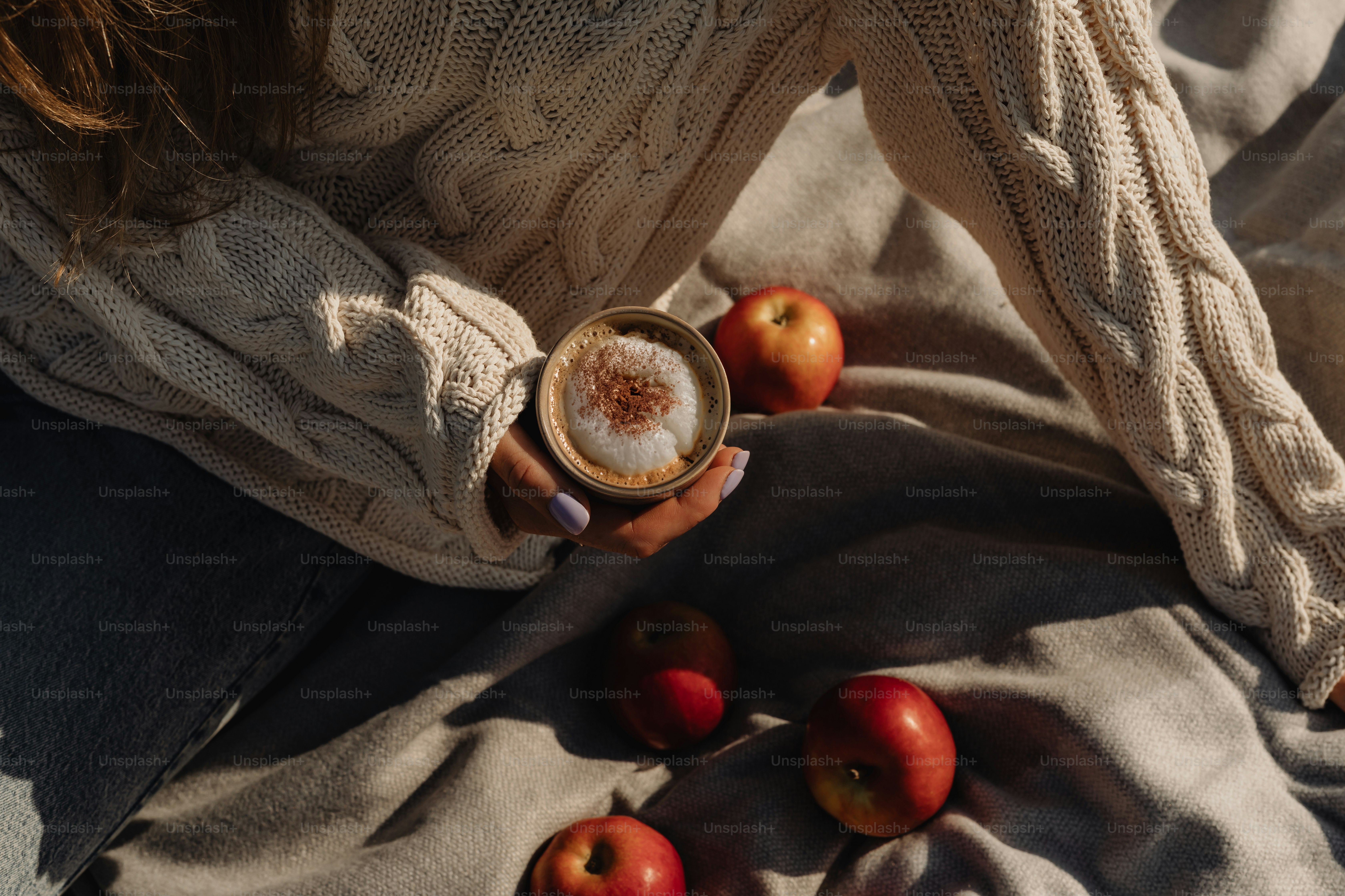 Una mujer sosteniendo una taza de café con manzanas a su alrededor