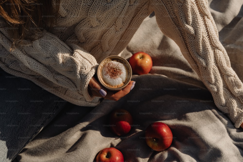 a woman holding a cup of coffee with apples around her