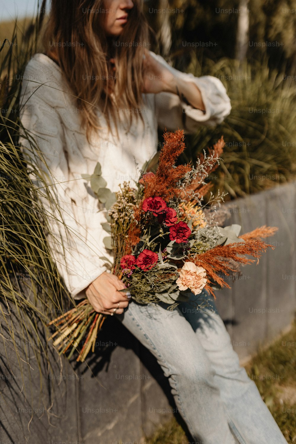 a woman sitting on a wall holding a bouquet of flowers