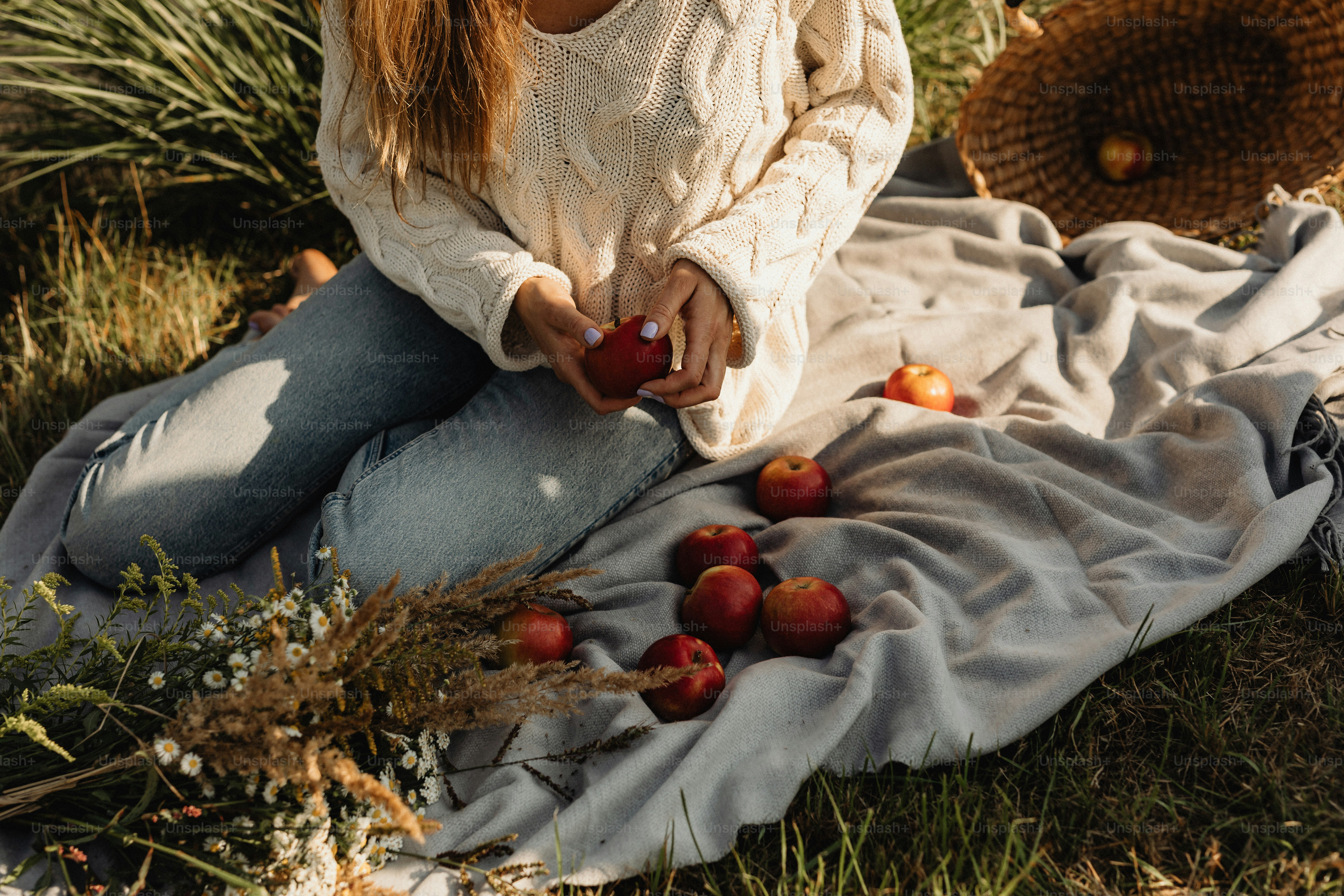 a woman sitting on a blanket with apples on the ground