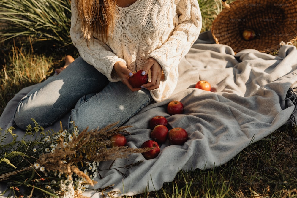 a woman sitting on a blanket with apples on the ground