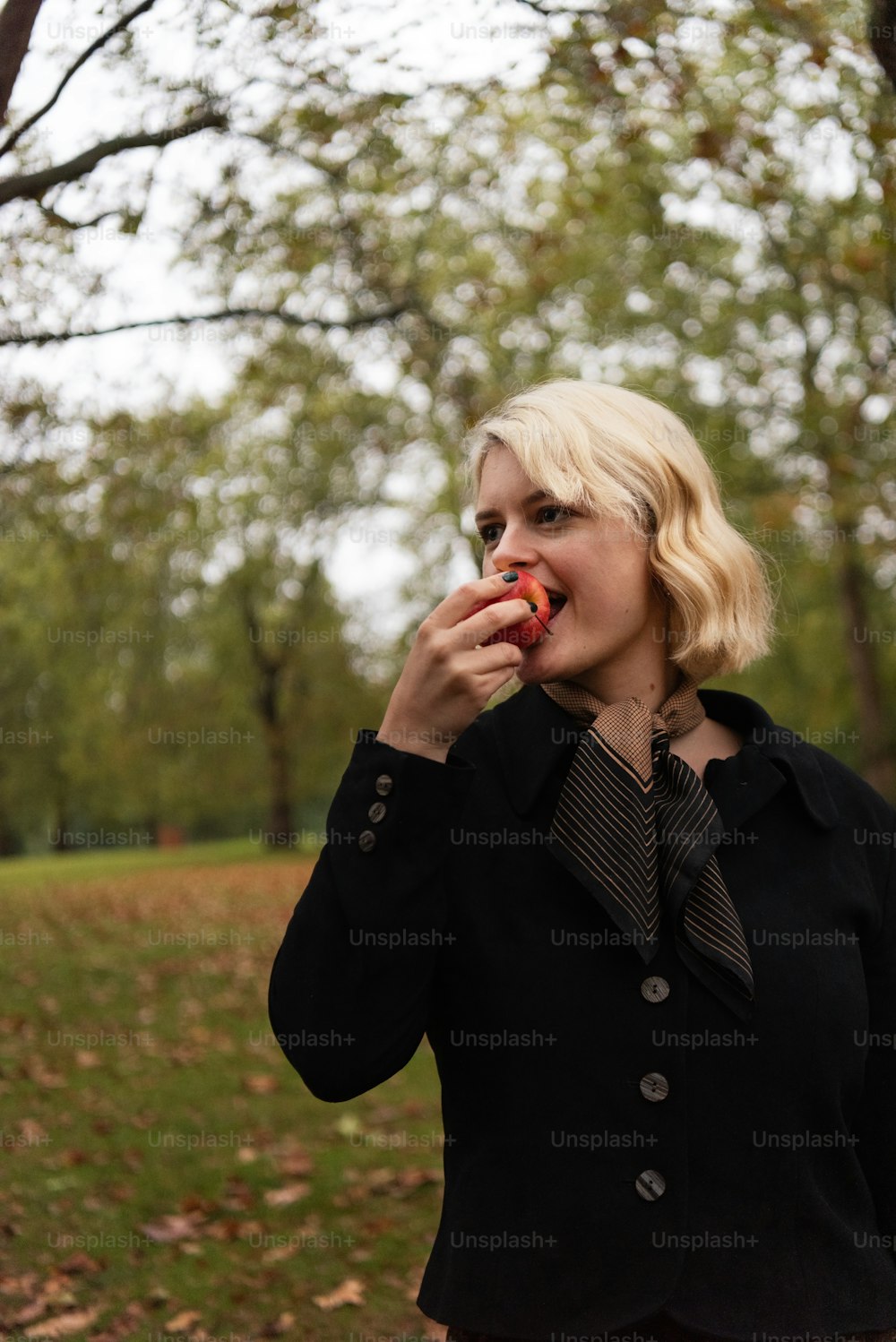 a woman in a black jacket eating an apple