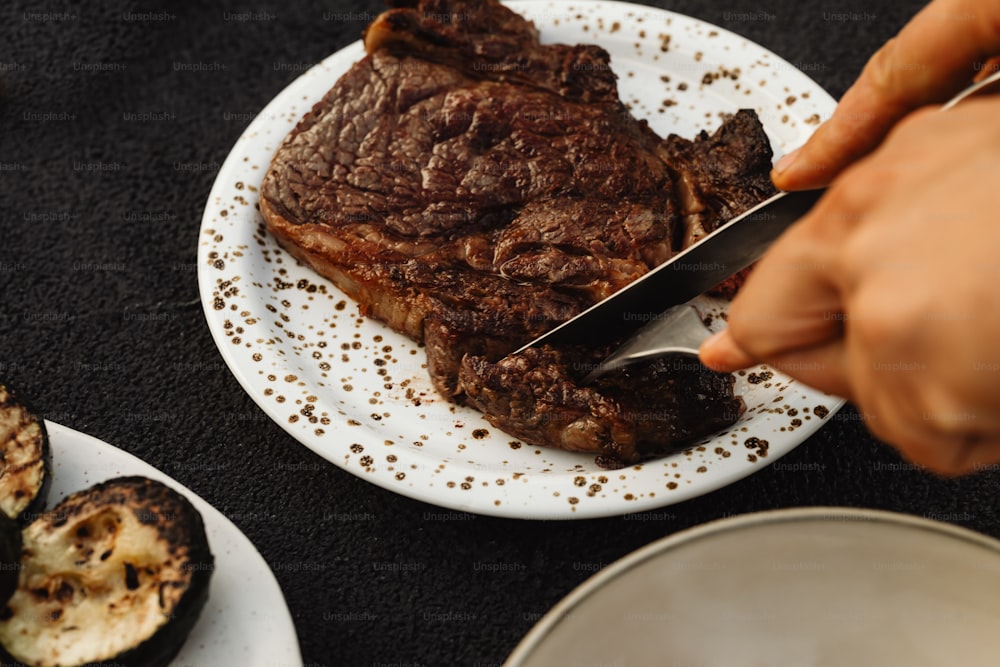 a person cutting a piece of steak on a plate