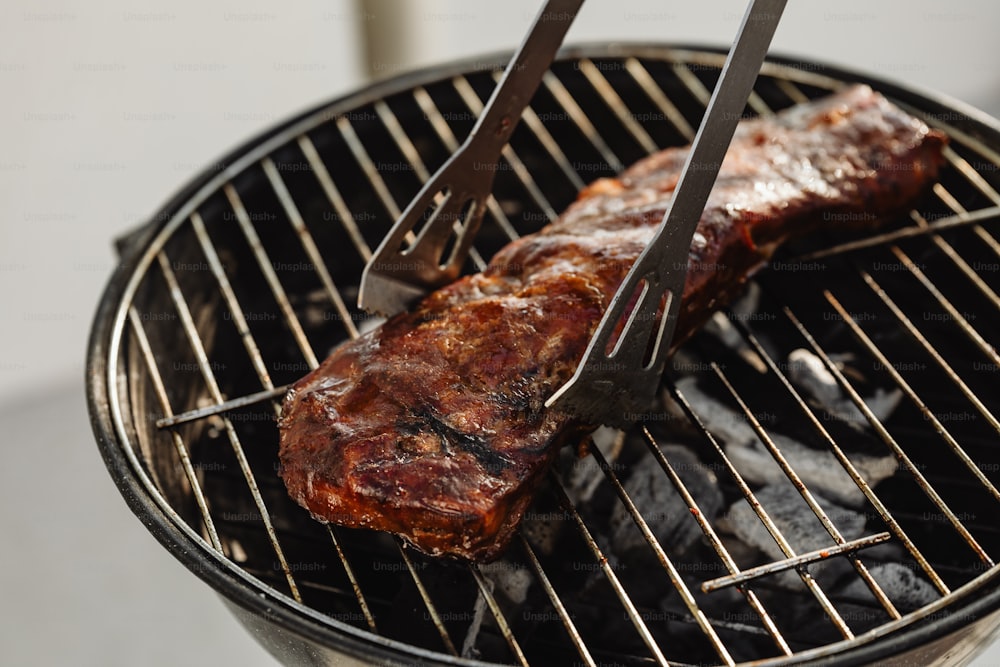 a steak being cooked on a grill with tongs