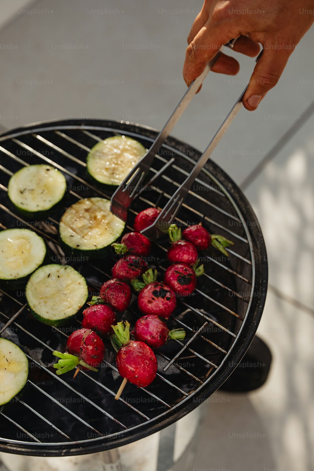 a person grilling food on a grill with strawberries and cucumbers