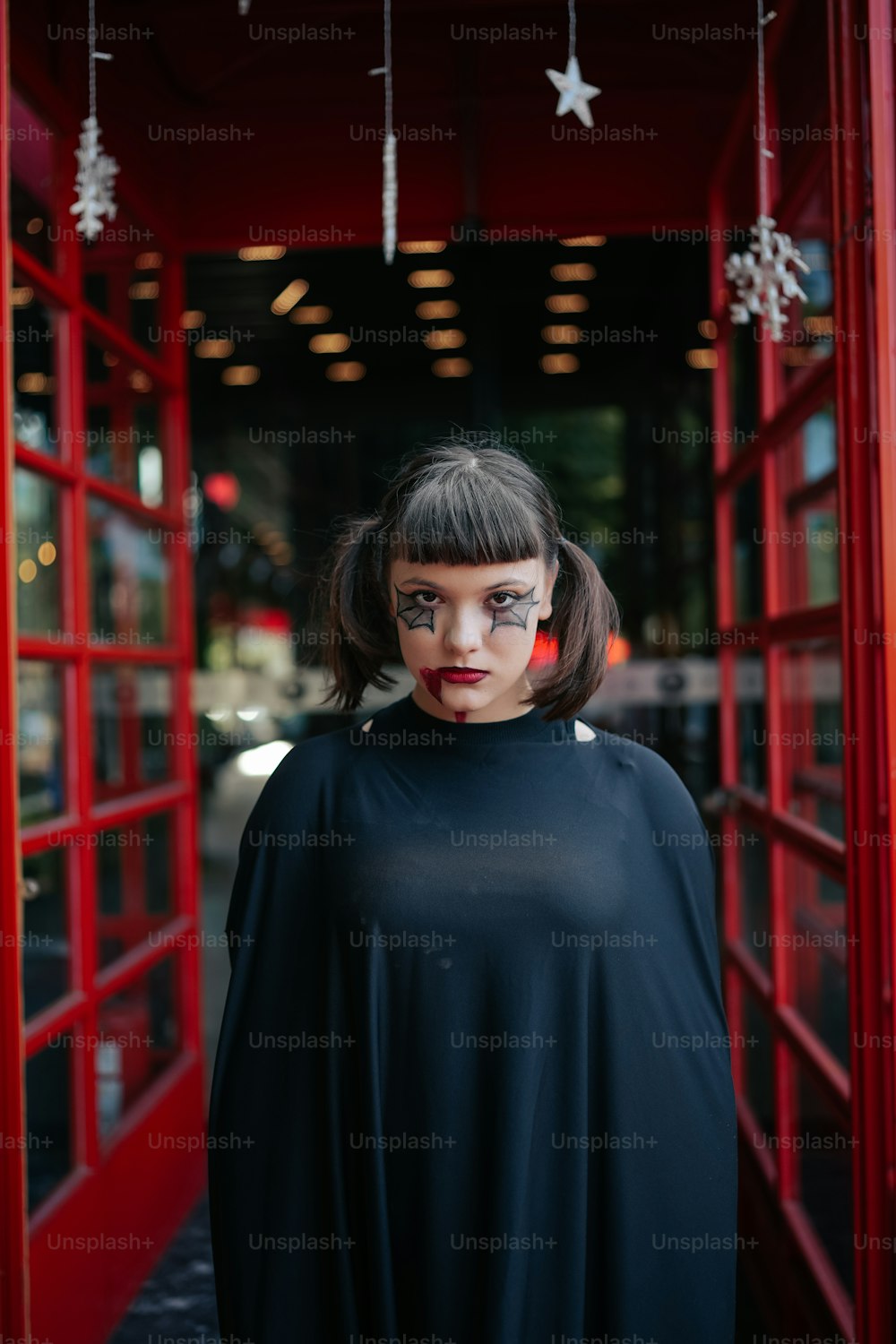 a woman in a black cape standing in front of a red phone booth
