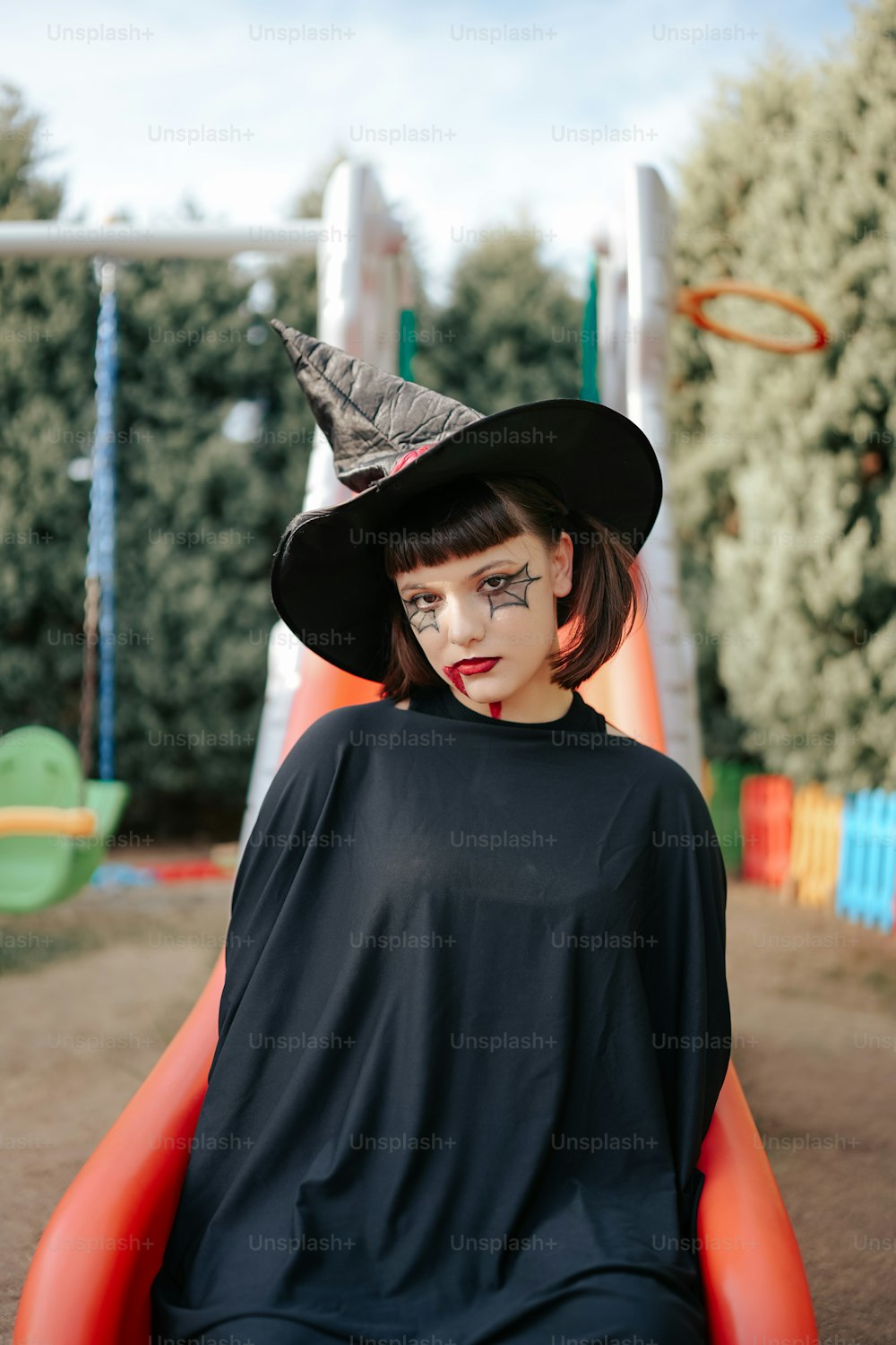 Une femme en costume de sorcière assise dans une cour de récréation