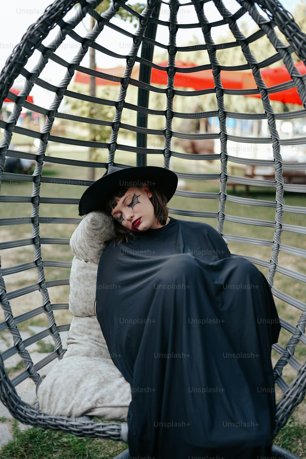 a woman in a black dress and hat sitting in a hammock