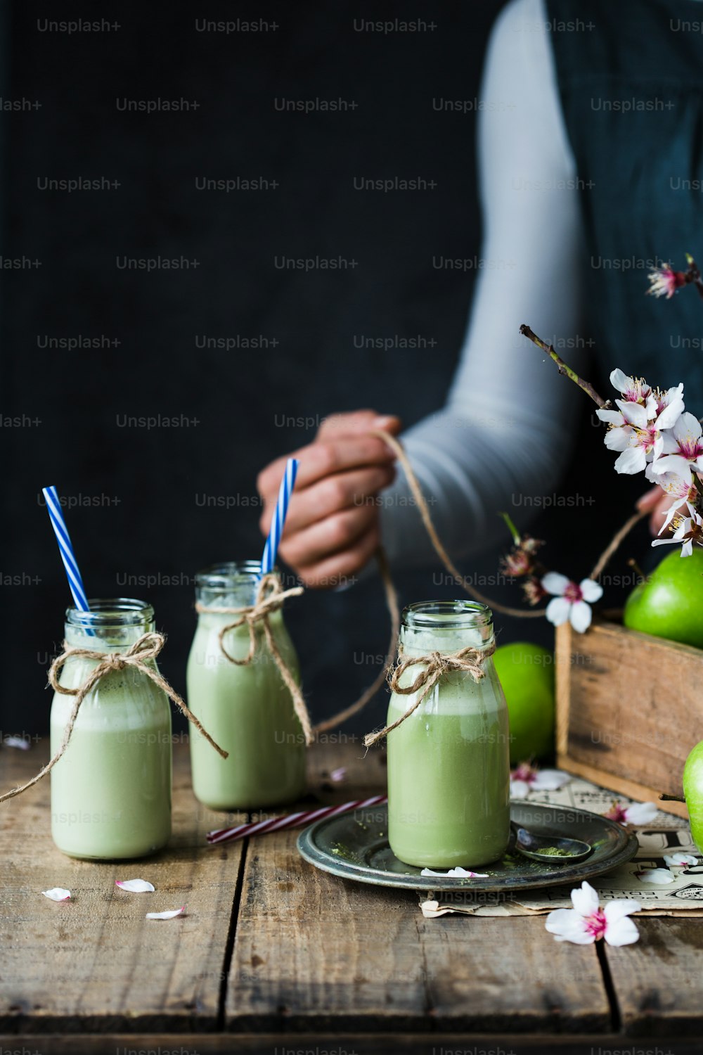 a person holding a straw in front of three jars filled with green liquid