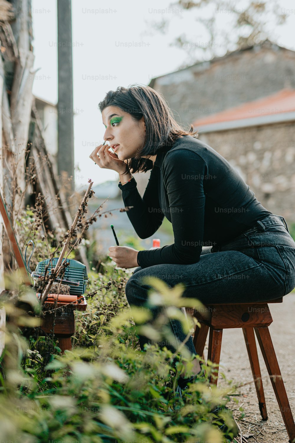 uma mulher sentada em um banquinho em frente a uma planta
