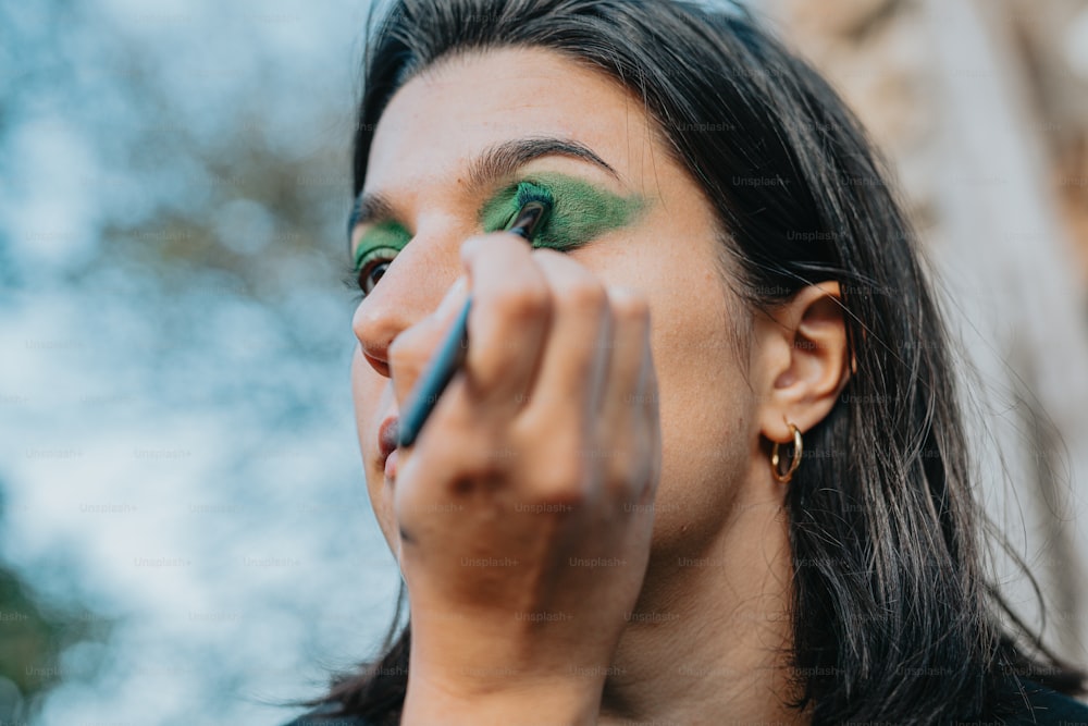 a woman with green eye makeup holding a pencil