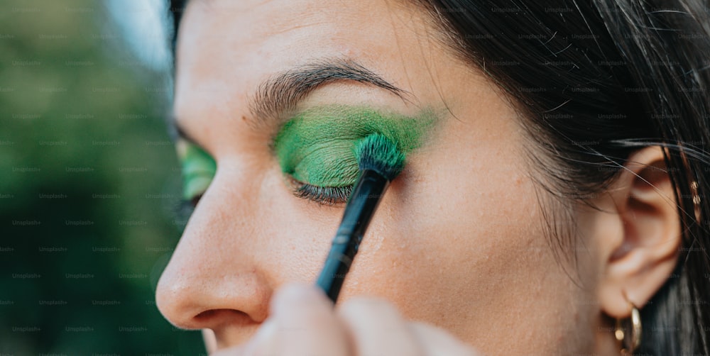a woman with a green eyeliner using a brush