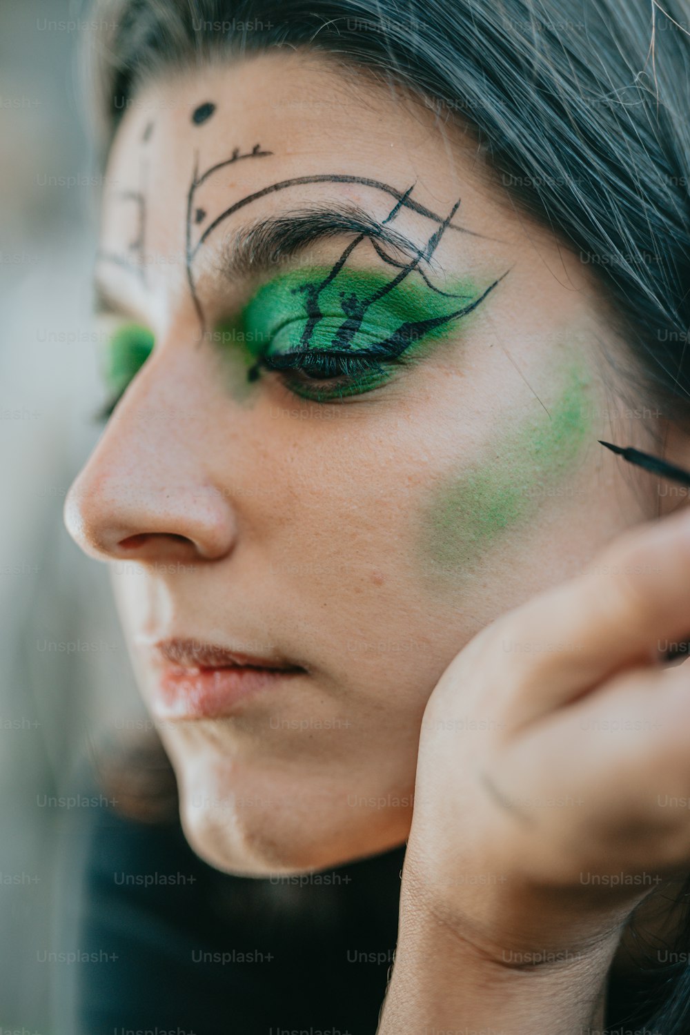 a woman with green eye makeup holding a cell phone