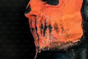un gros plan du visage d’un homme avec de la peinture orange et noire dessus