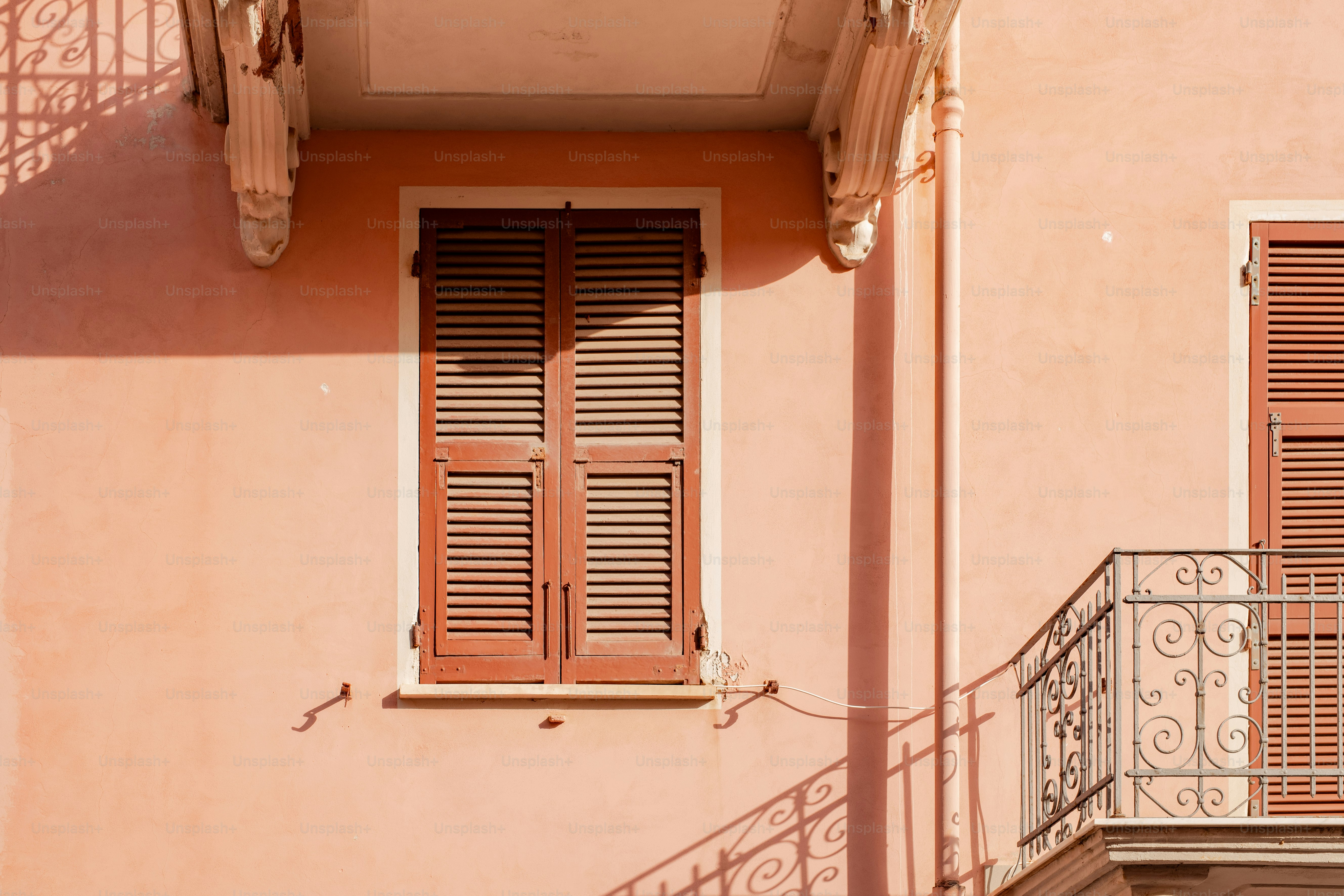 a pink building with a balcony and two windows