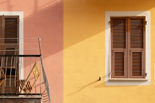 a yellow building with a balcony and a window with shutters
