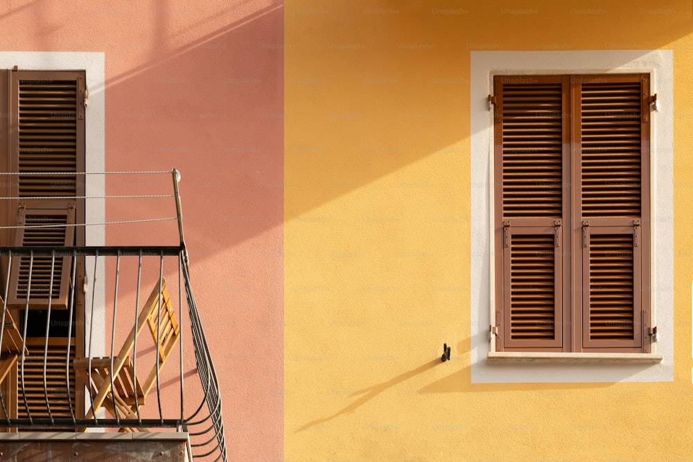 a yellow building with a balcony and a window with shutters