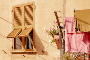 a window with a wooden shutter and a pink towel on a clothes line