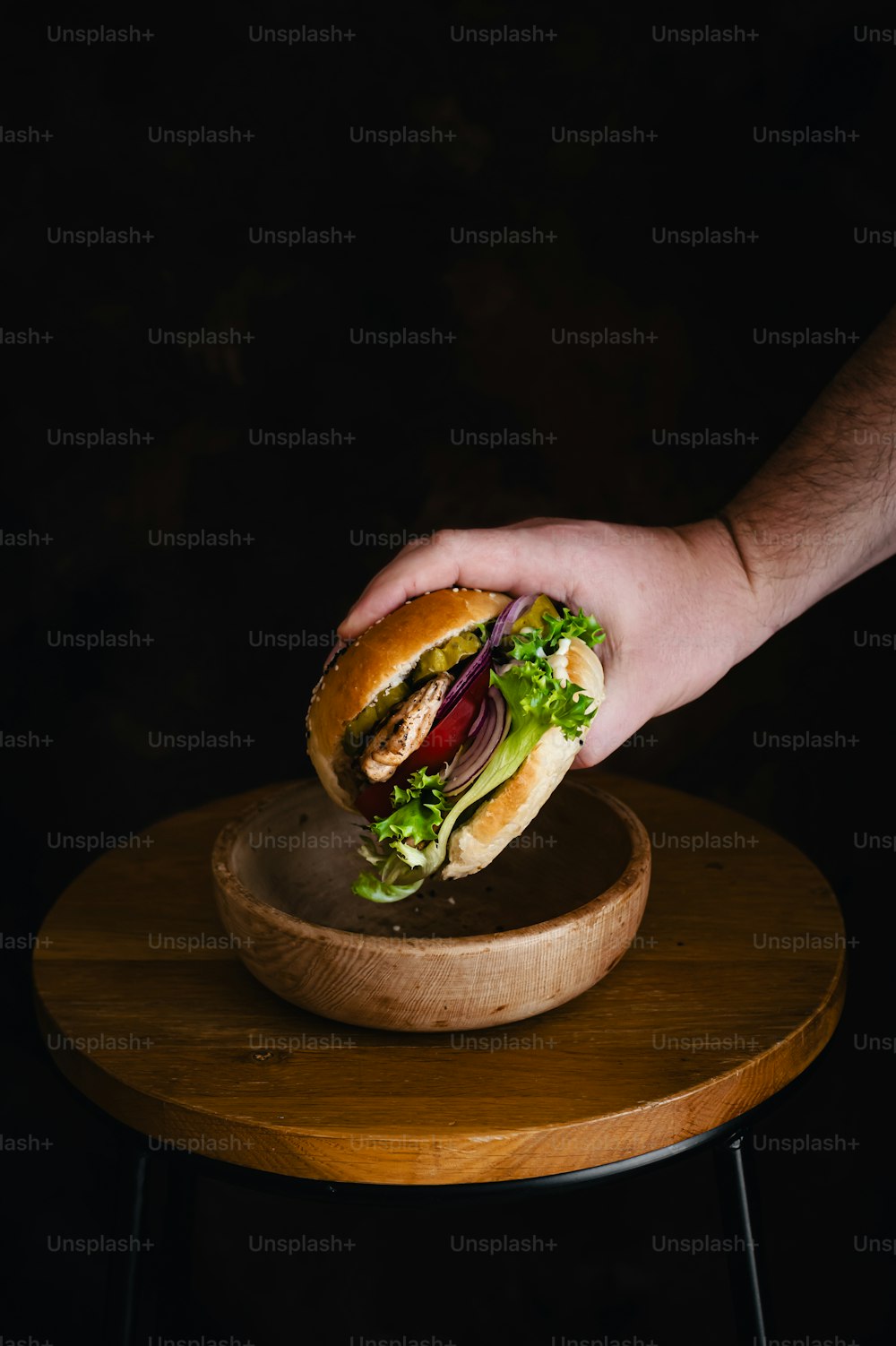 a hand holding a sandwich on top of a wooden plate