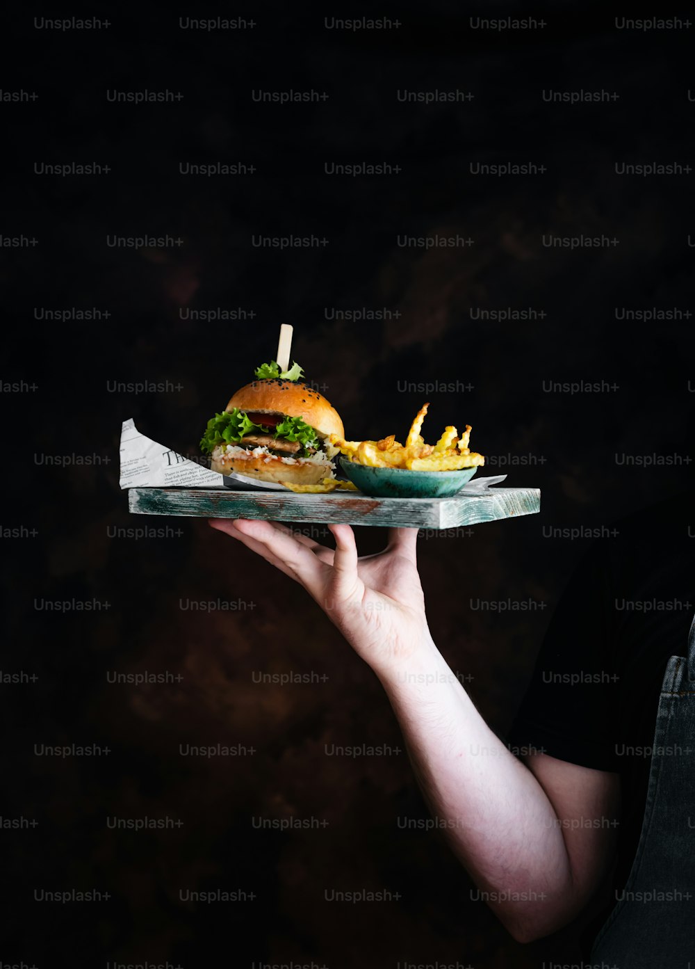 a person holding a tray with a sandwich and fries on it