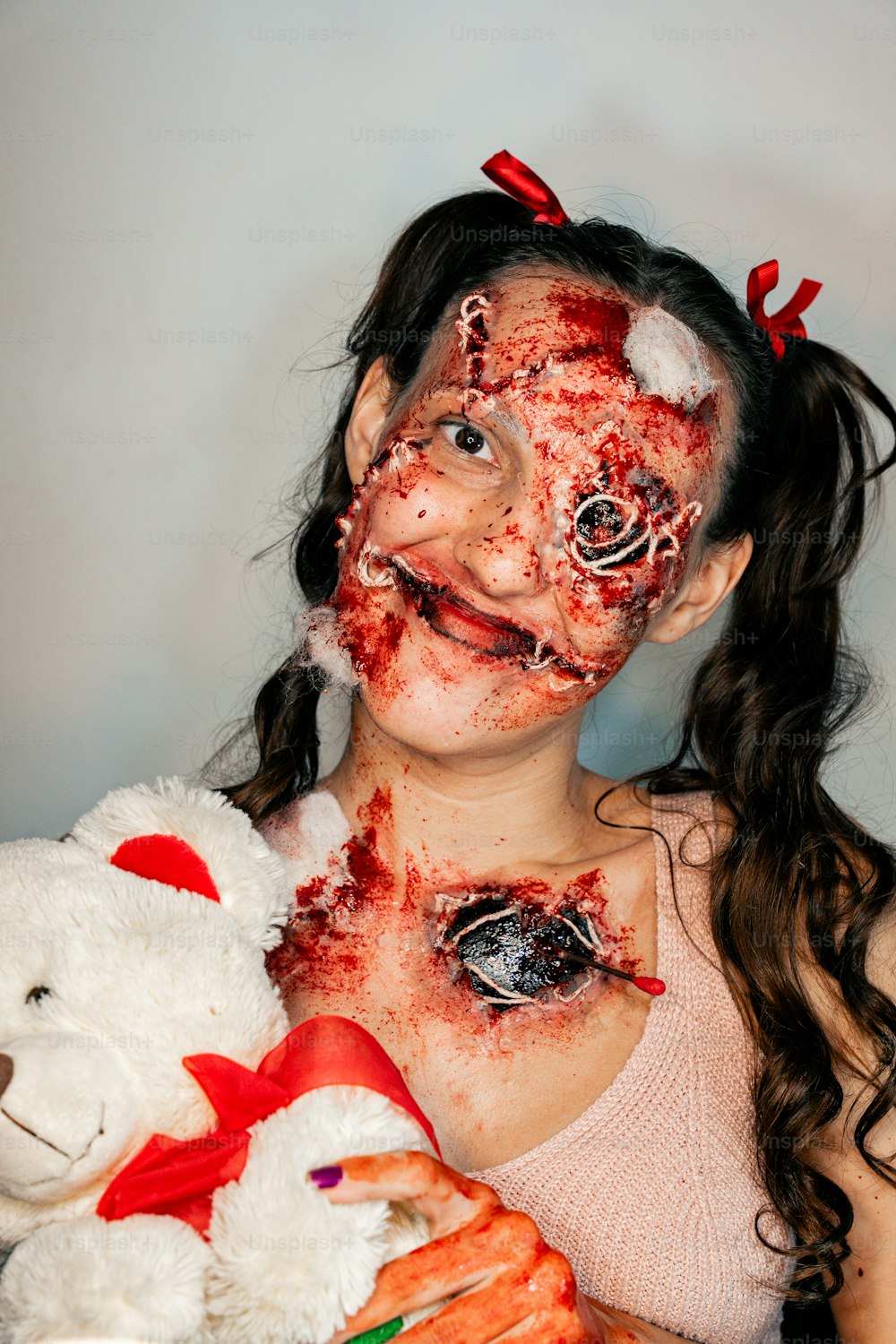 Una niña con sangre en toda la cara sosteniendo un oso de peluche