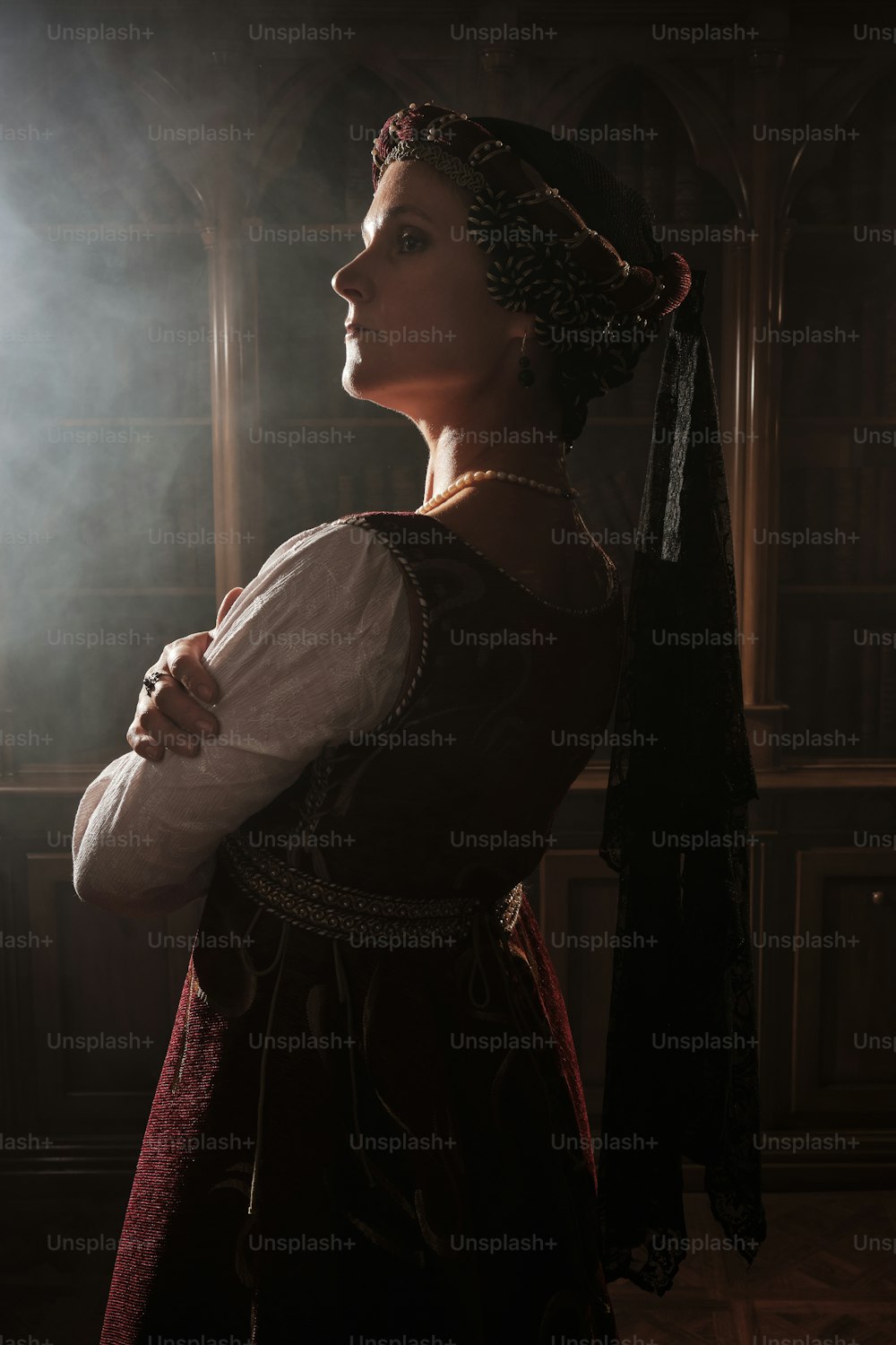 uma mulher em um vestido renascentista em pé em um quarto escuro