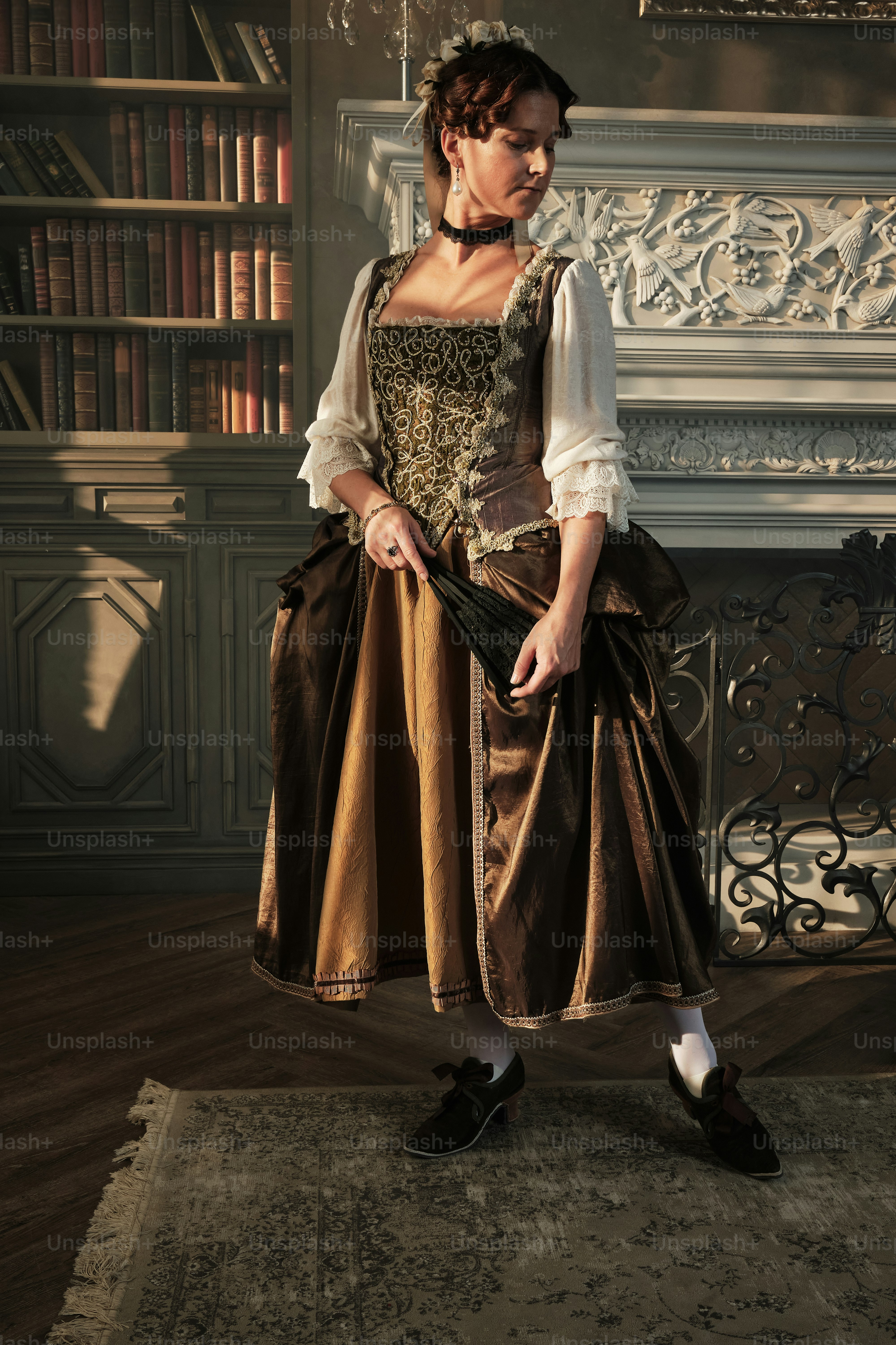 a woman in a brown dress standing in front of a fireplace