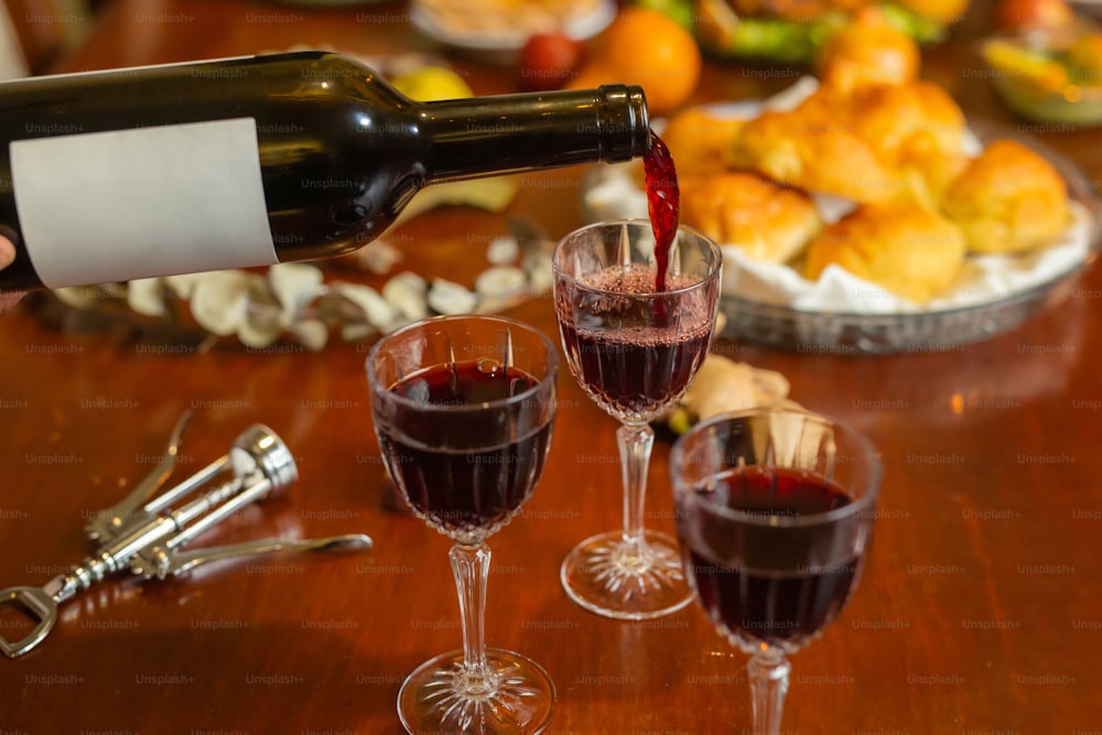 a person pouring red wine into wine glasses