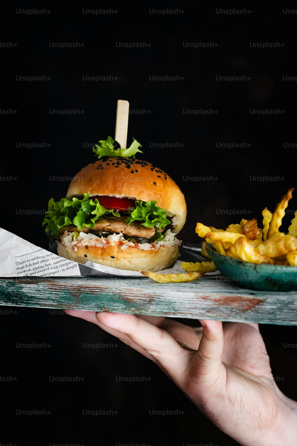 a hand holding a tray with a burger and fries